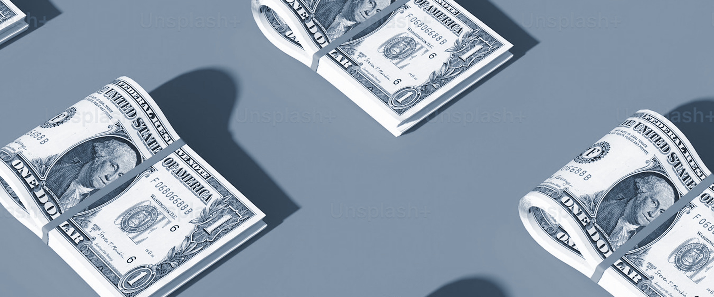 Rolled and bundled US dollar bills on a gray surface, representing the cost of hiring a web developer and software development budgeting in 2026.